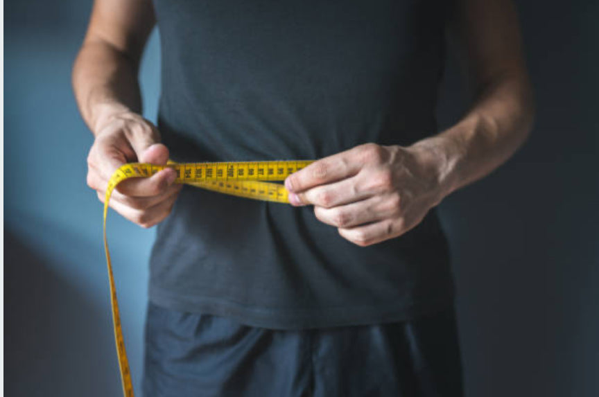 Clothed man measuring his waist with measuring tape 